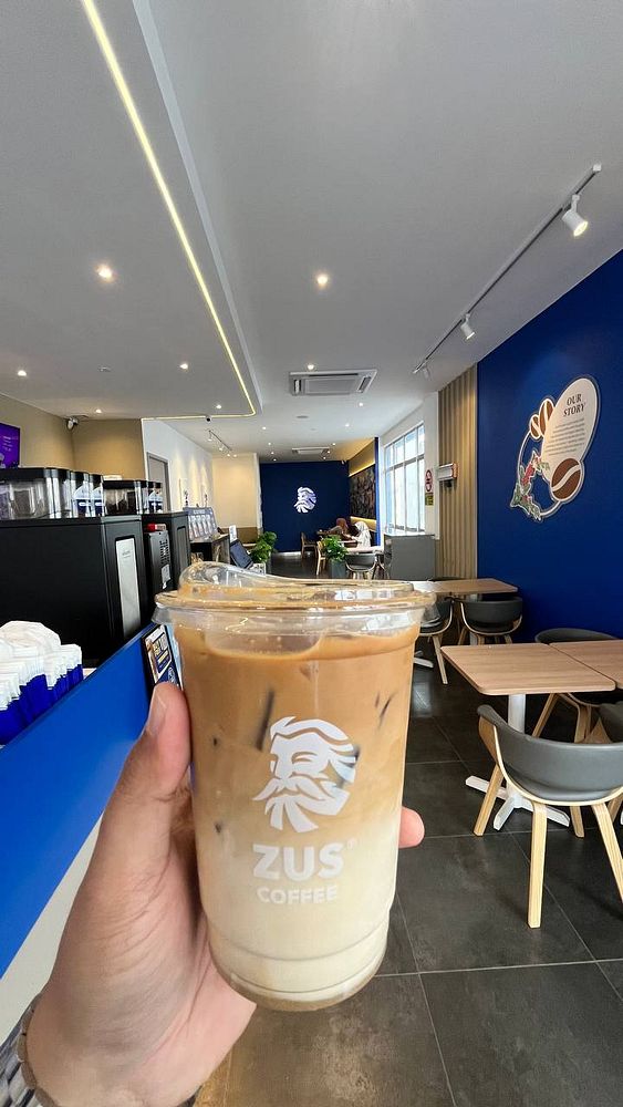 Hand holding an iced coffee cup inside a modern coffee shop with blue-themed interior decor.