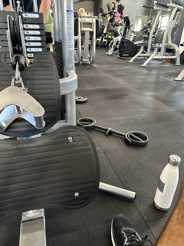 The image captures a gym environment with workout equipment and a water bottle.