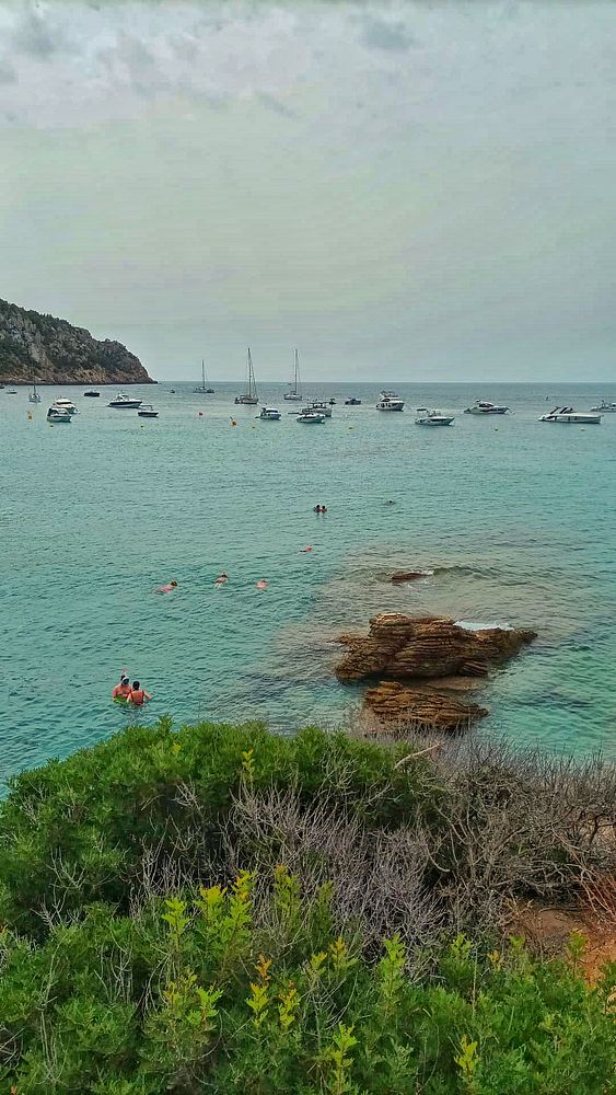 A serene beach scene on a cloudy Sunday with boats in the water and people swimming.