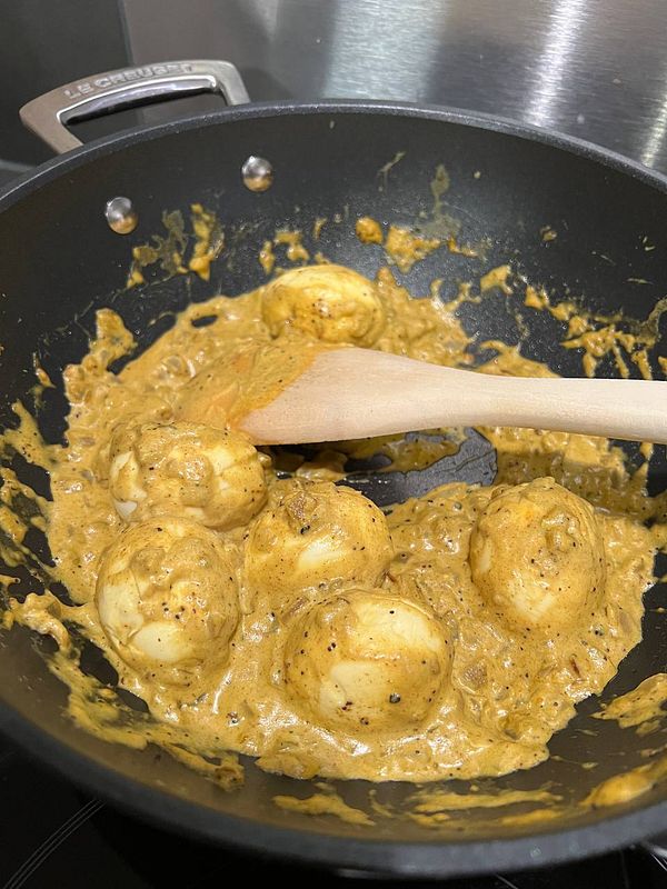 A pot of creamy curry with boiled eggs is being prepared on a stovetop.