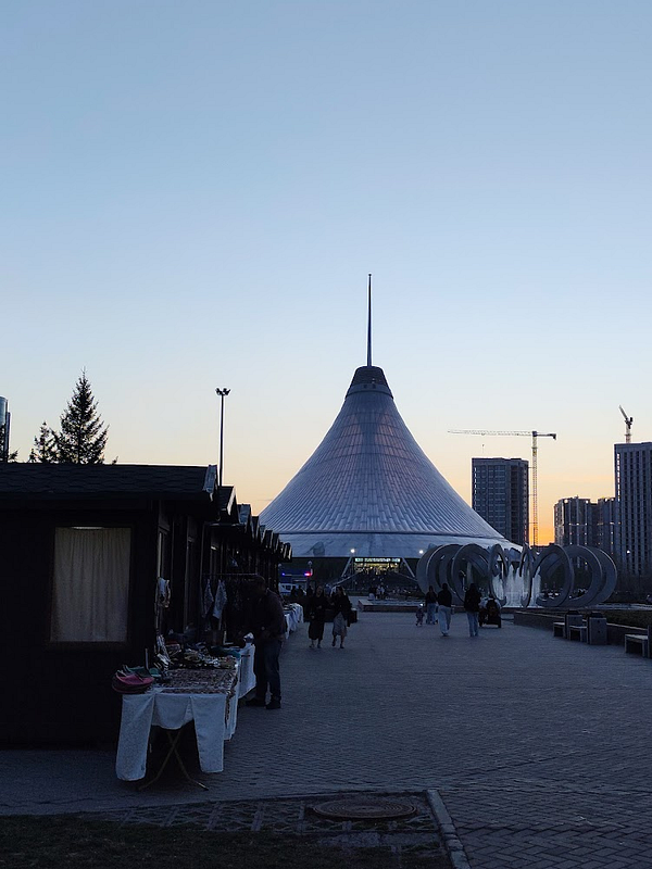 A man walks with his dog along a quiet pathway near water during evening golden hour.