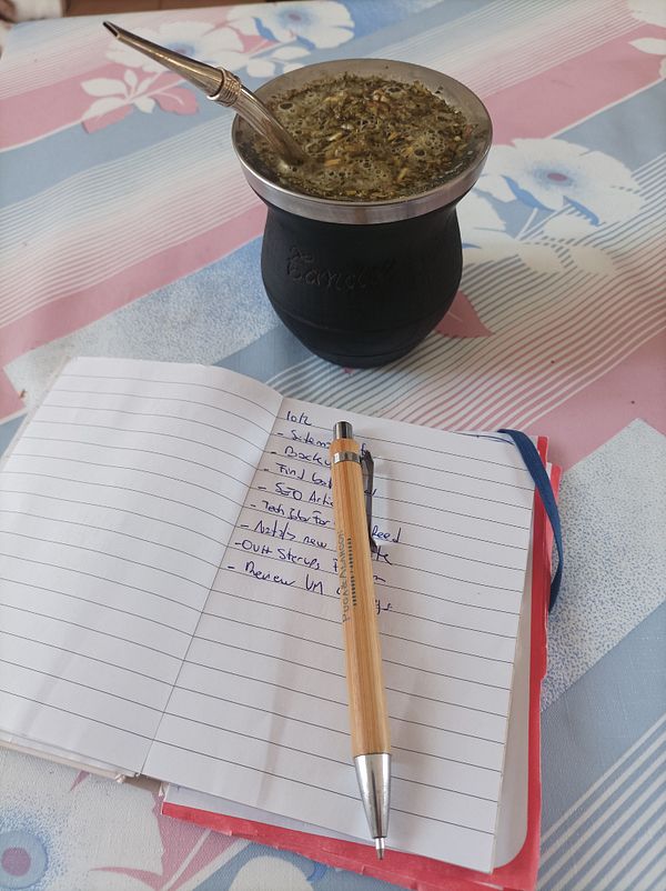 A traditional mate drink is placed next to a notebook filled with tasks.