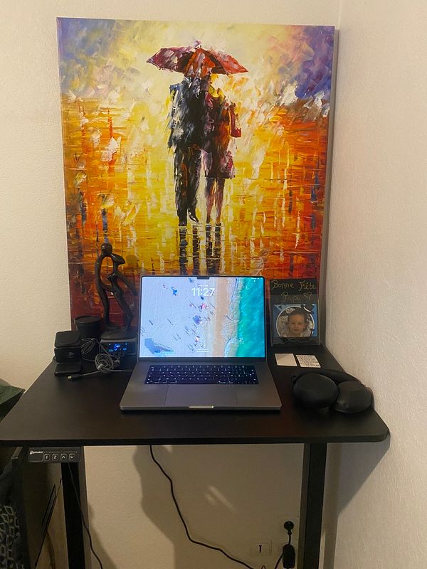 A clean standing desk with a laptop, headphones, a decorative art piece, and a framed photo in a corner setup.