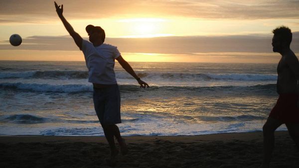 Two individuals are playing with a ball on the beach during sunset.