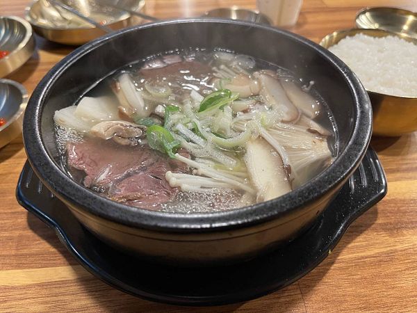 A steaming bowl of soup with various ingredients is presented on a wooden table.