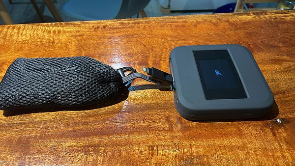 Desk setup with an Anker 5G wifi router powered by a portable Anker backup battery, alongside a laptop and informal items, illustrating a backup internet solution during a power outage.