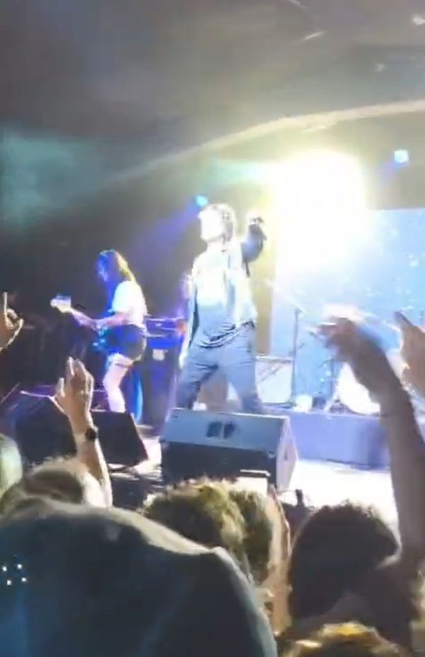 A vibrant live rock concert scene with a lead singer and guitarist performing on stage, and an enthusiastic crowd raising hands in front.