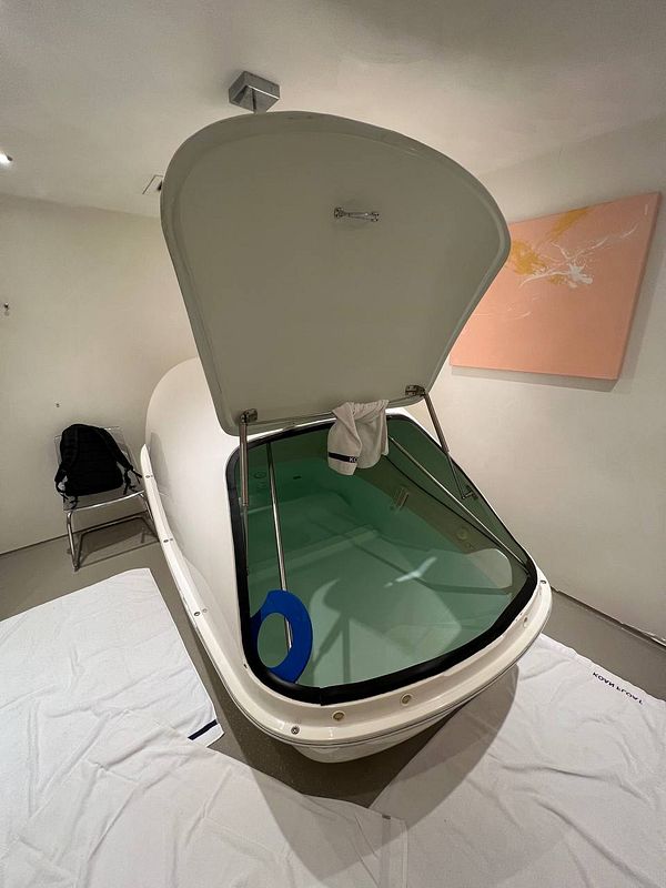 The image depicts a floatation tank in a serene, minimalist room.