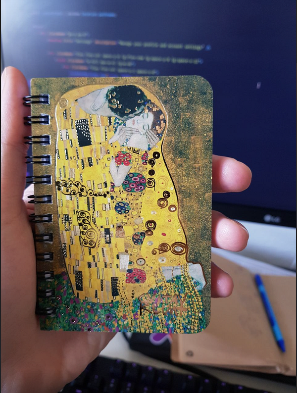 A hand holds a small notebook featuring a famous painting design.