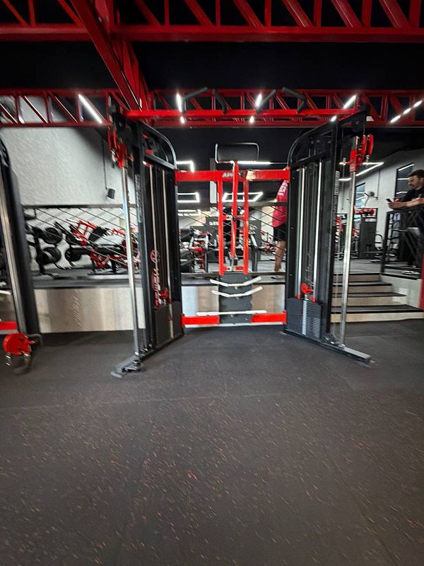A fit young man lifts a dumbbell in a modern gym setting with rich wood accents and large windows.