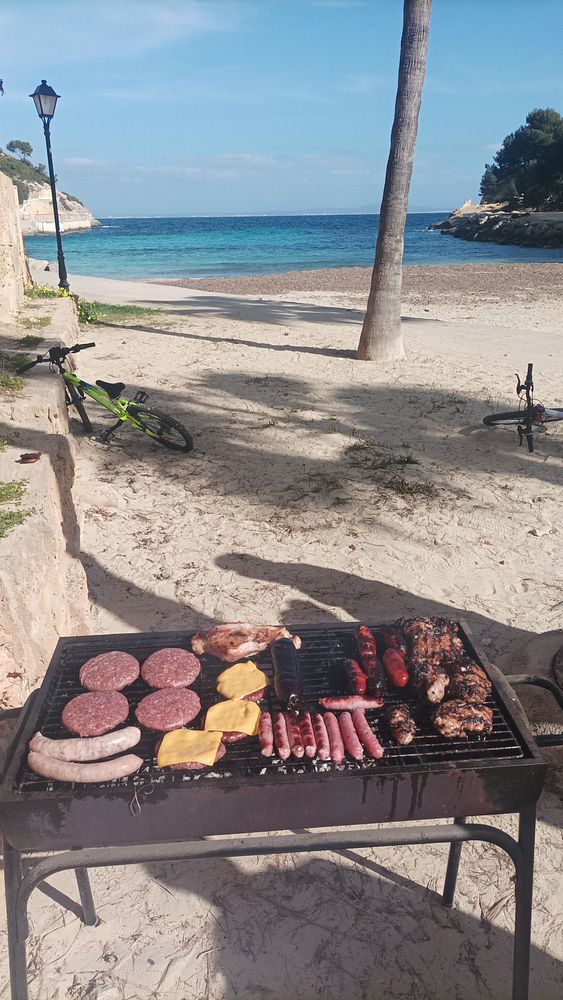 A beachside barbecue setup with various meats grilling on a barbecue grill.