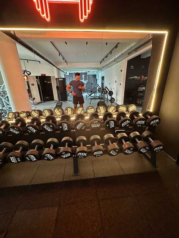 A gym interior featuring a rack of dumbbells and a person reflected in a mirror.