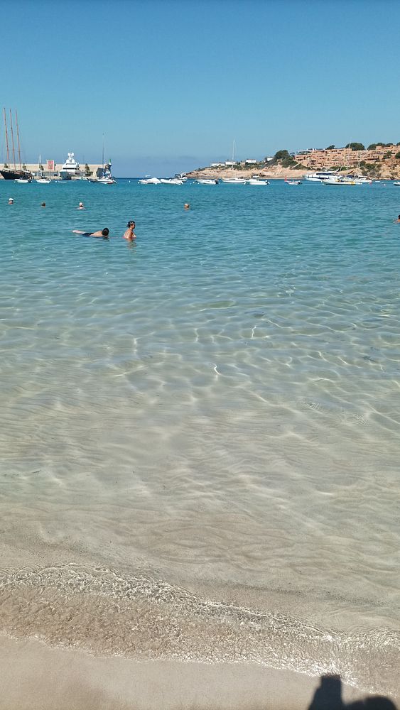 A serene beach scene with people swimming in clear turquoise water.