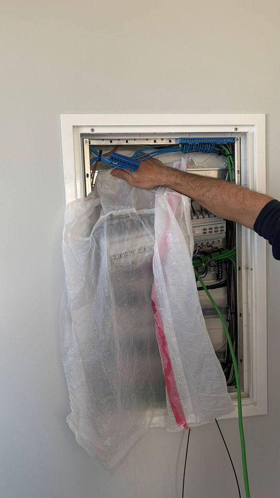 An electrician is inspecting an electrical box covered with a plastic sheet to prevent water damage.