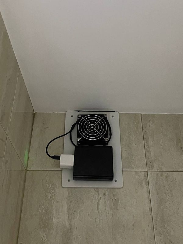 A mounted ventilation system with a fan and power supply is installed on a wall.