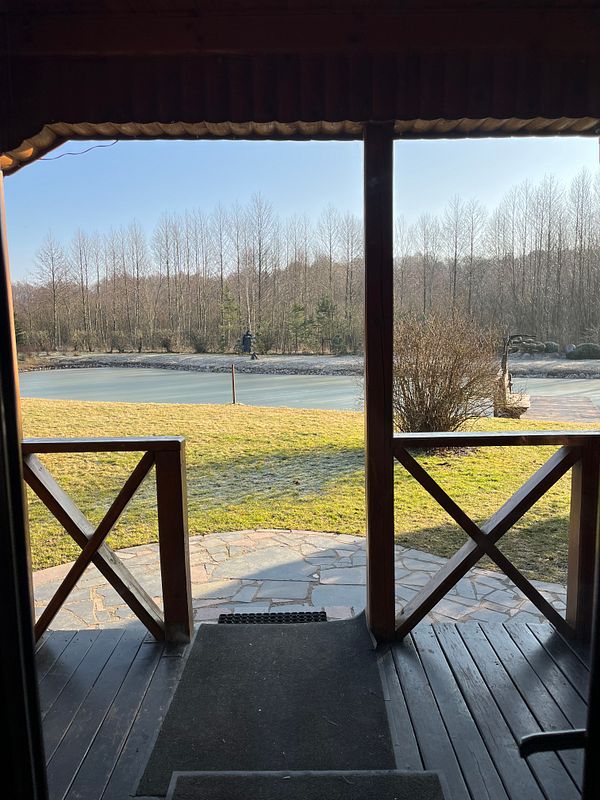 A serene outdoor view from a cabin porch overlooking a frozen lake and trees.