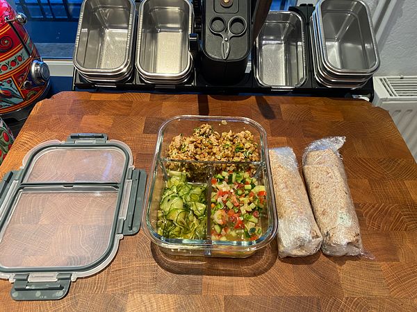 A neatly organized meal prep setup featuring a glass container with food and wrapped items on a wooden countertop.