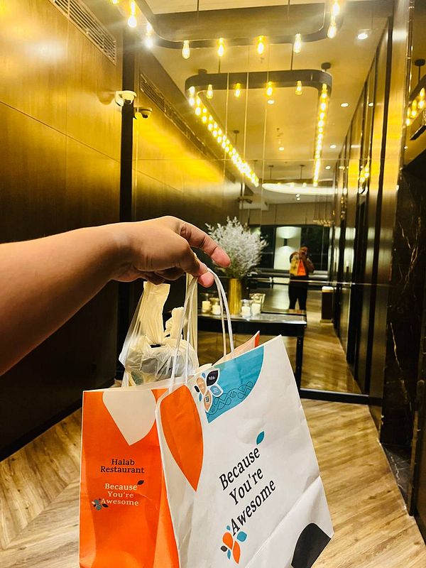 A person is holding two takeaway bags in a stylish hotel corridor.