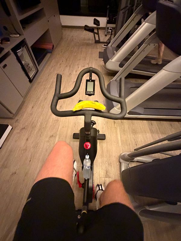 A young man performing an overhead triceps extension exercise with a dumbbell in a gym.