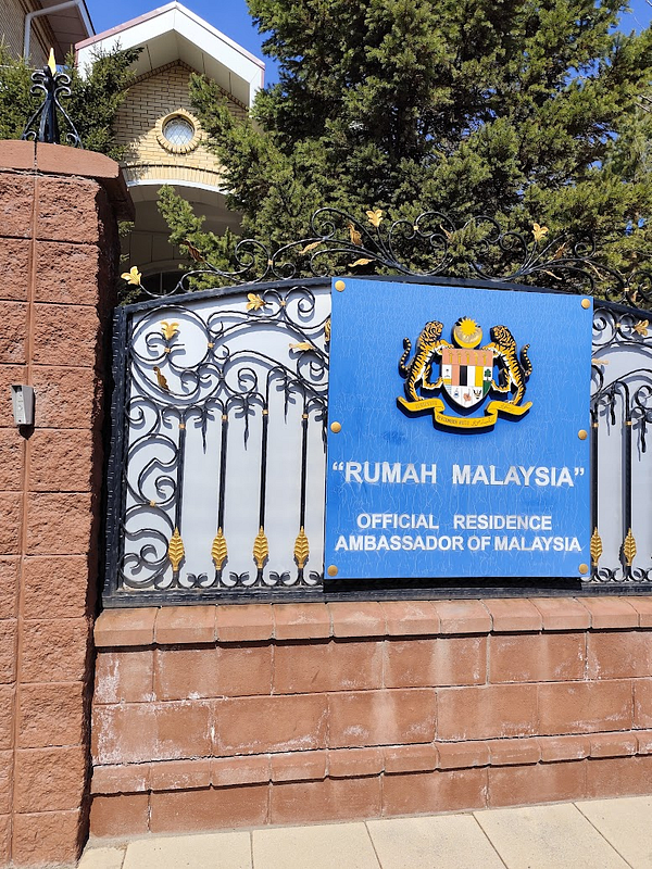 The image features the entrance gate of the Malaysian Embassy in Astana, Kazakhstan.