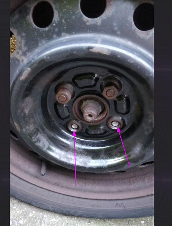The image depicts a close-up view of a car wheel hub with broken wheel studs.
