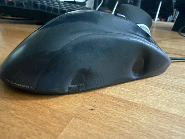 A worn-out black computer mouse is resting on a wooden desk.
