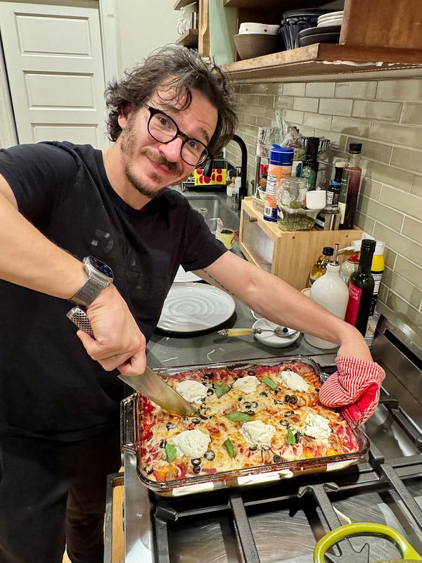 A homemade focaccia pizza topped with fresh basil leaves and sliced red peppers on a white plate.