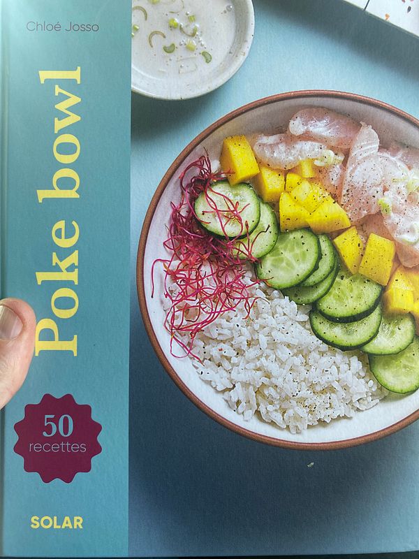 A hand holds a cookbook titled 'Poke Bowl' featuring a colorful poke bowl recipe.