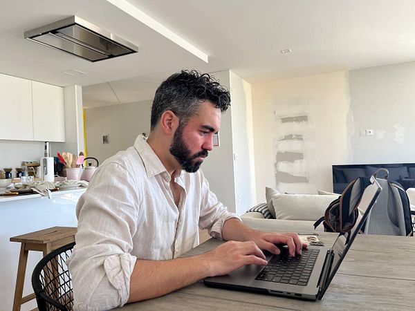 A man is focused on working at a laptop in a modern, partially furnished living space.