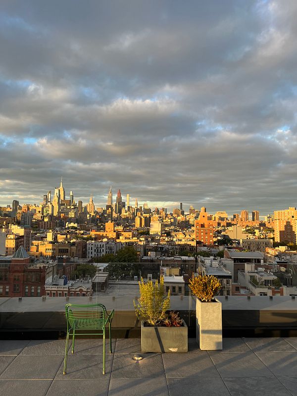 A stunning rooftop view of a city skyline during sunset, featuring a green chair and potted plants in the foreground.