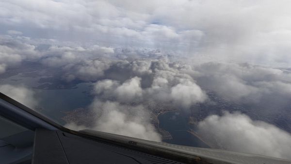View from an airplane window showing a white airplane wing and engine under cloudy skies during a storm.