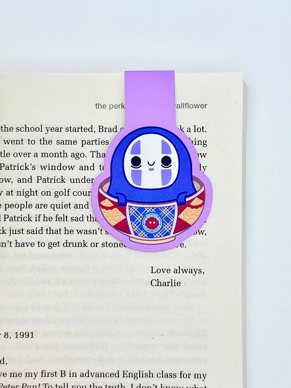 A colorful magnetic bookmark featuring a cute character is placed on an open book page.