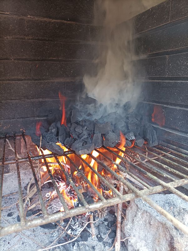 A charcoal grill is lit with flames and smoke rising from burning coals.