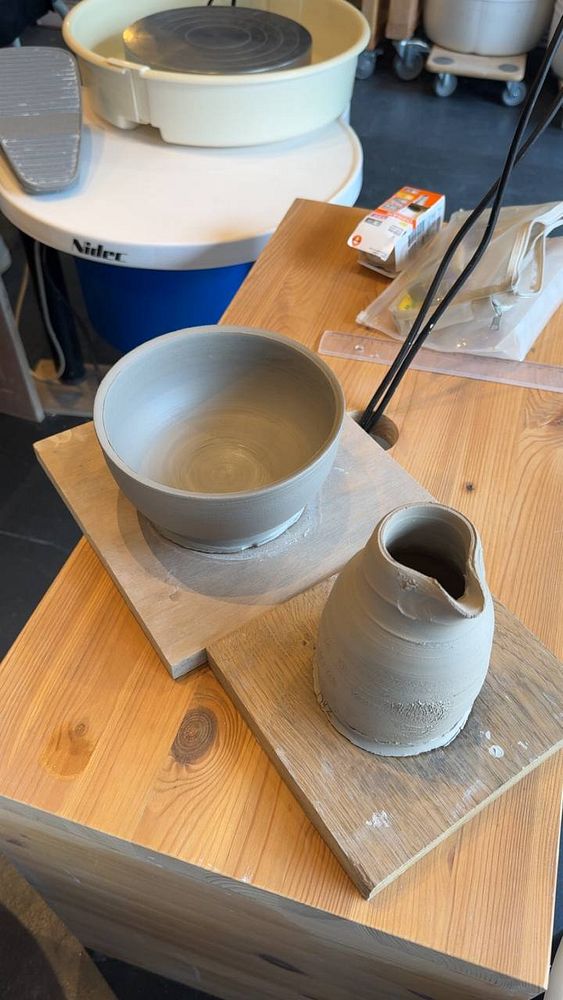 A ceramic mug of coffee in a vibrant blue glaze sits on a wooden table next to a small flower arrangement, with cozy indoor lighting in the background.