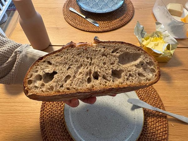 A hand holds a freshly sliced loaf of sourdough bread, showcasing its airy interior.
