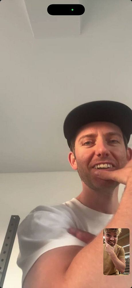 Two men engaged in a video call, with one man visibly flexing his arm in a casual setting.