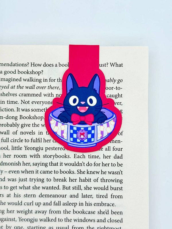 A colorful magnetic bookmark featuring a cartoon cat design is placed on an open book page.