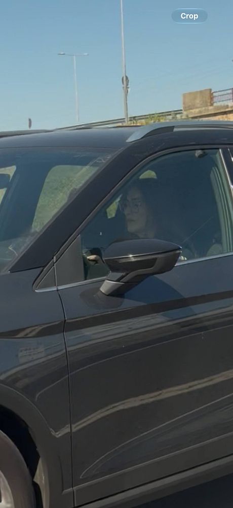A woman driving a dark-colored car focused on her phone while on a highway.