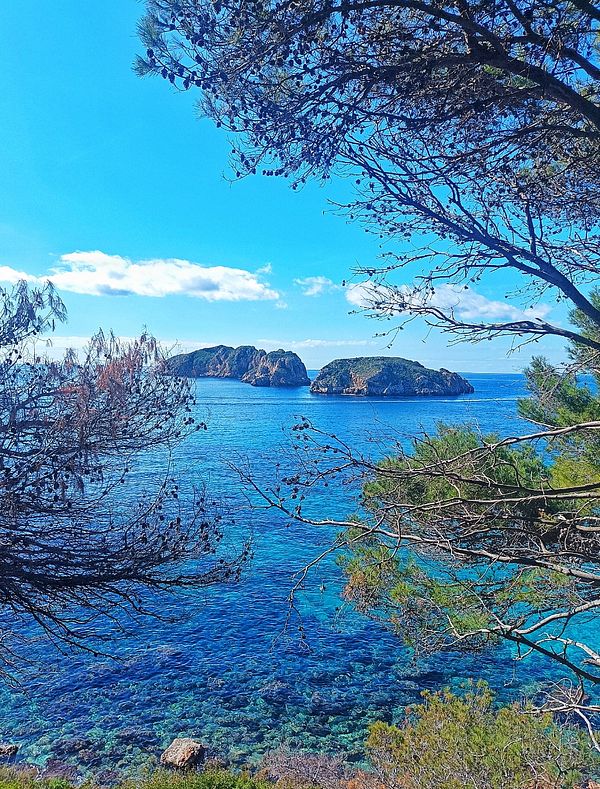 A scenic view of two islands surrounded by clear blue water, framed by trees.