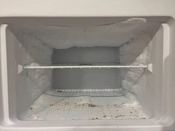 The image depicts a freezer with significant ice buildup and debris on the bottom.