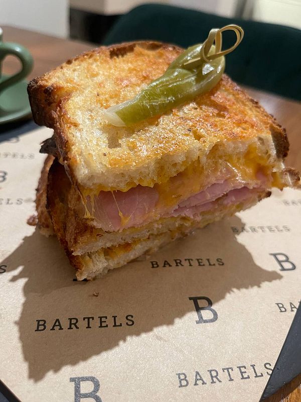 A grilled cheese sandwich with ham is presented on a branded paper at a restaurant.