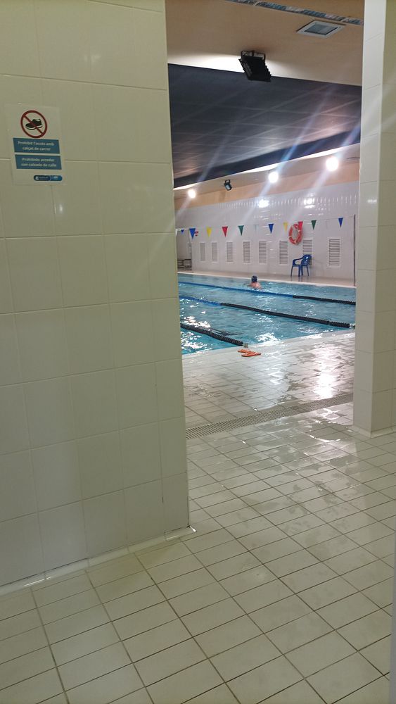The image captures the view of an indoor swimming pool area from a tiled hallway.