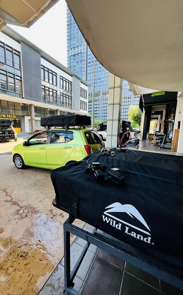 A vibrant green car is parked under a covered area, with a rooftop cargo box and various equipment visible nearby.