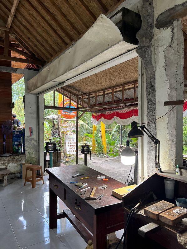 The image depicts a workshop space designed for silver crafting, featuring tools and an open view to the outdoors.