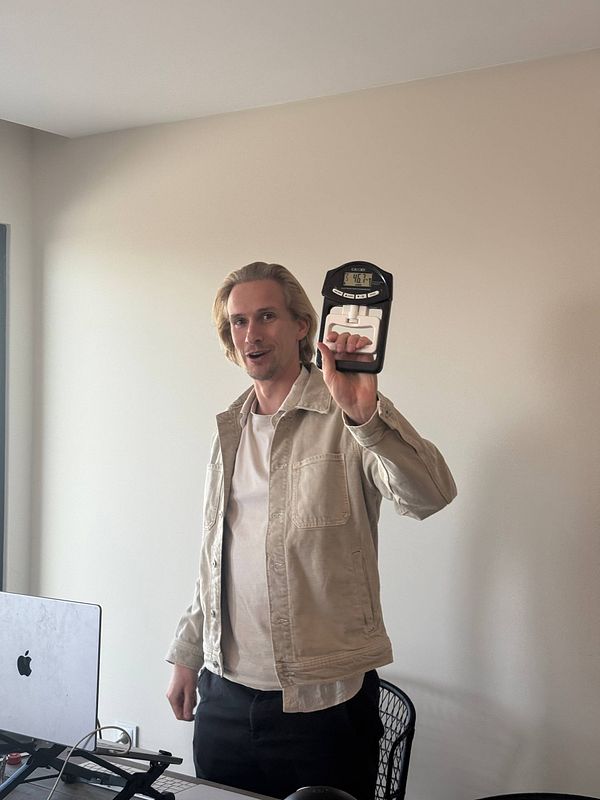 A man is holding a digital hand dynamometer while smiling in a coworking space.