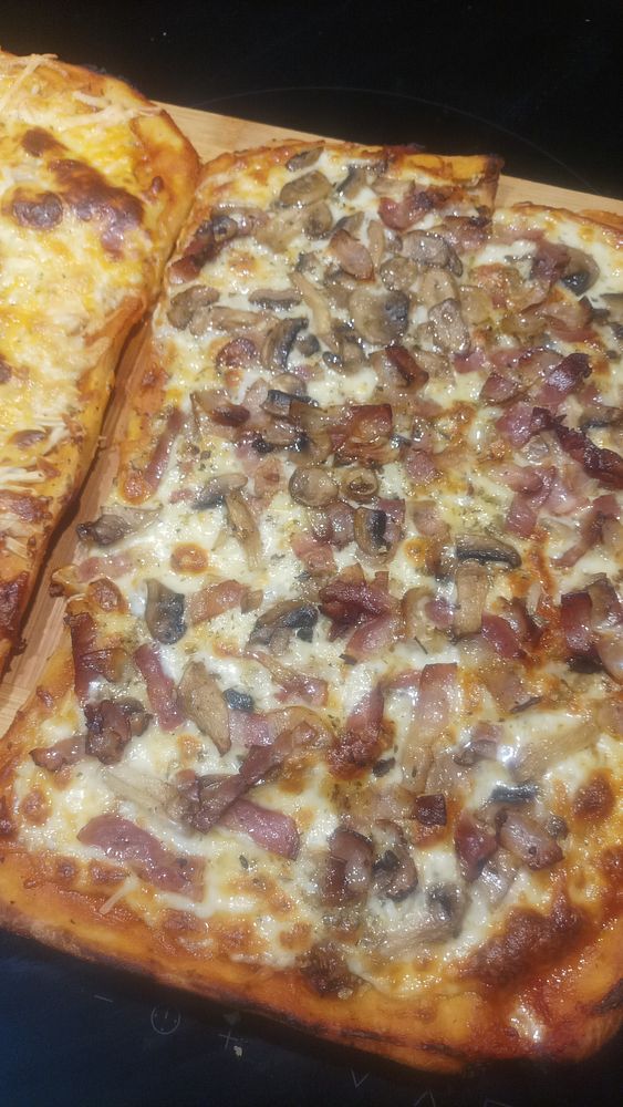 Close-up of a homemade pizza with various toppings including tomatoes, olives, and herbs.