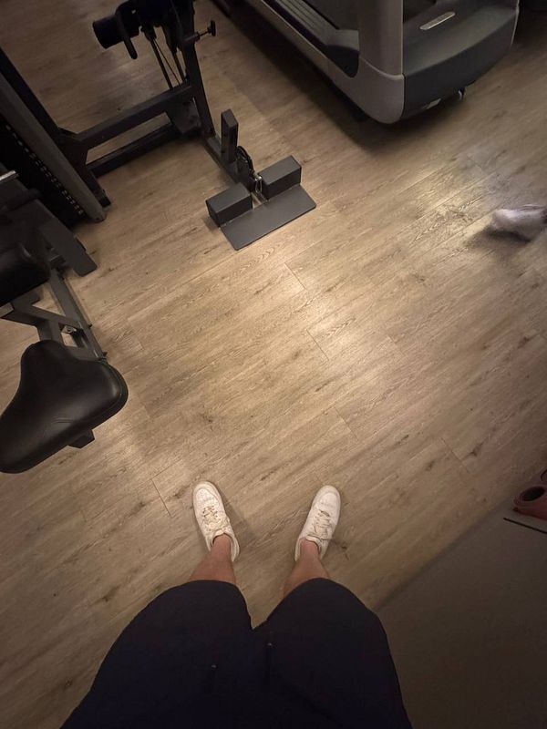 The image captures a person's legs and feet in a gym setting.