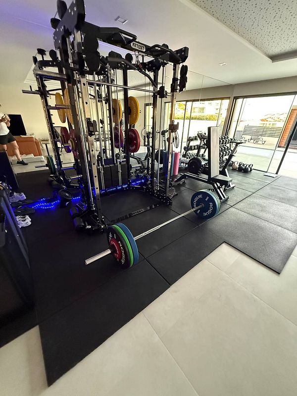 A well-equipped home gym featuring various weightlifting equipment and a spacious layout.