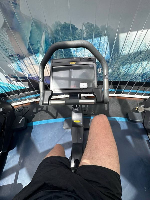 A person is seated on a stationary bike in a gym with a scenic backdrop.