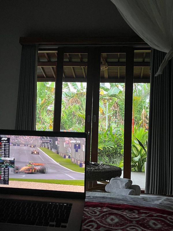 A cozy indoor setting with a laptop displaying an F1 race and a lush outdoor view.